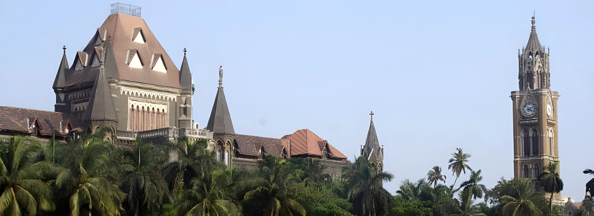 A grand structure with a clock tower in Mumbai, prominently displaying a clock, set against a bright blue sky.