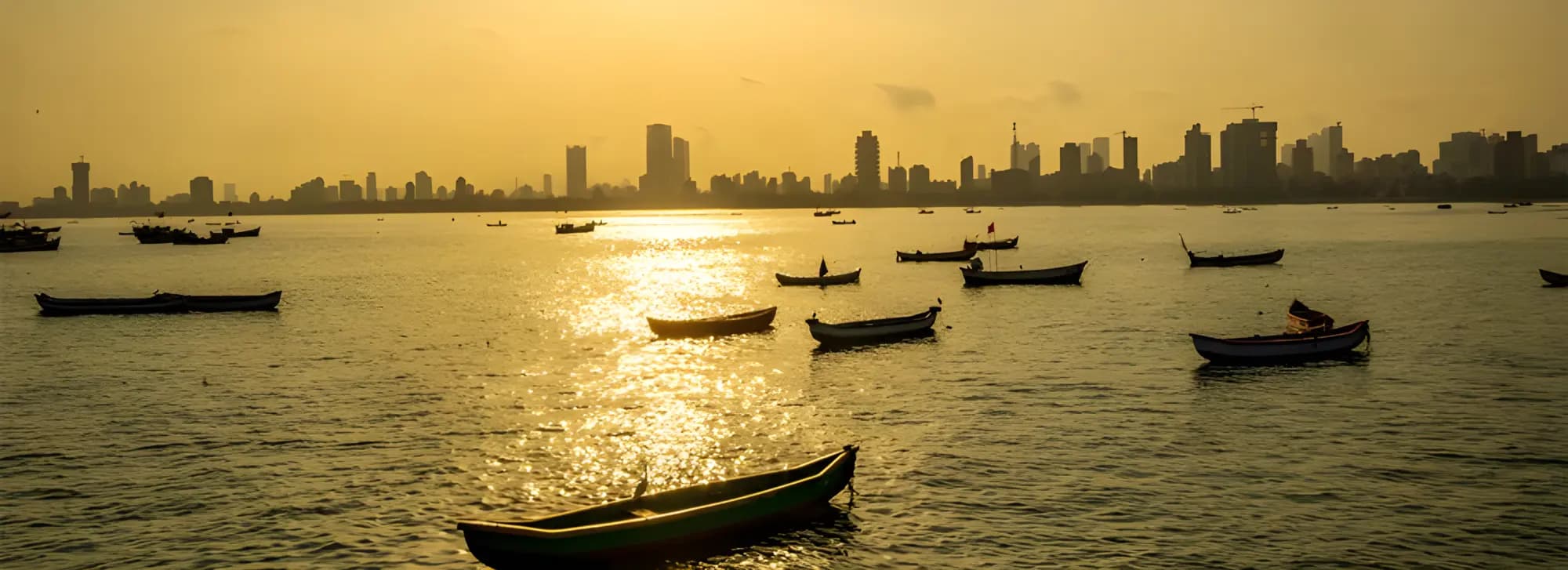 A serene view of boats on water with a sunset backdrop, embodying the beauty of a Mumbai tour experience.